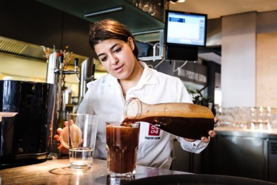 Mitarbeiterin füllt vorsichtig Kaffee in ein Glas.